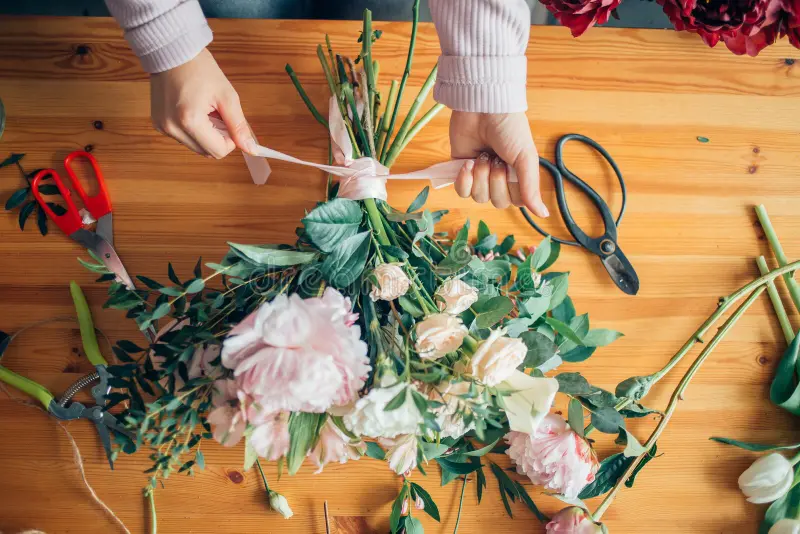 Close-up of hands carefully arranging fresh flowers with scissors and greenery on a wooden workbench